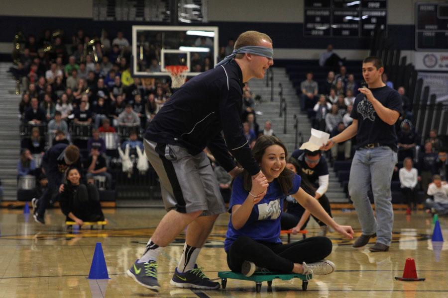 Junior Mitch Perkins and junior Logan Marney participate in a blindfolded race on scooters against the freshman, sophomore, and senior classes at the winter homecoming pep assembly on Friday, Jan. 17.