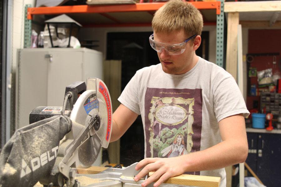 Junior Elijah Sheahan saws wood to the correct dimensions in order to complete the frame for the spring play sets on Thursday, Feb. 27. [In Set Crew] we rebuild off of existing sets, Sheahan said. It is a fun way to make friends and prepare for the future. 