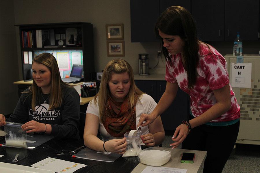 Acting as a teacher in the class Teaching as a Career on Thursday, April 24, senior Madison Thomas teaches junior Caitlin Alley how to make ice cream in a bag for a class project.