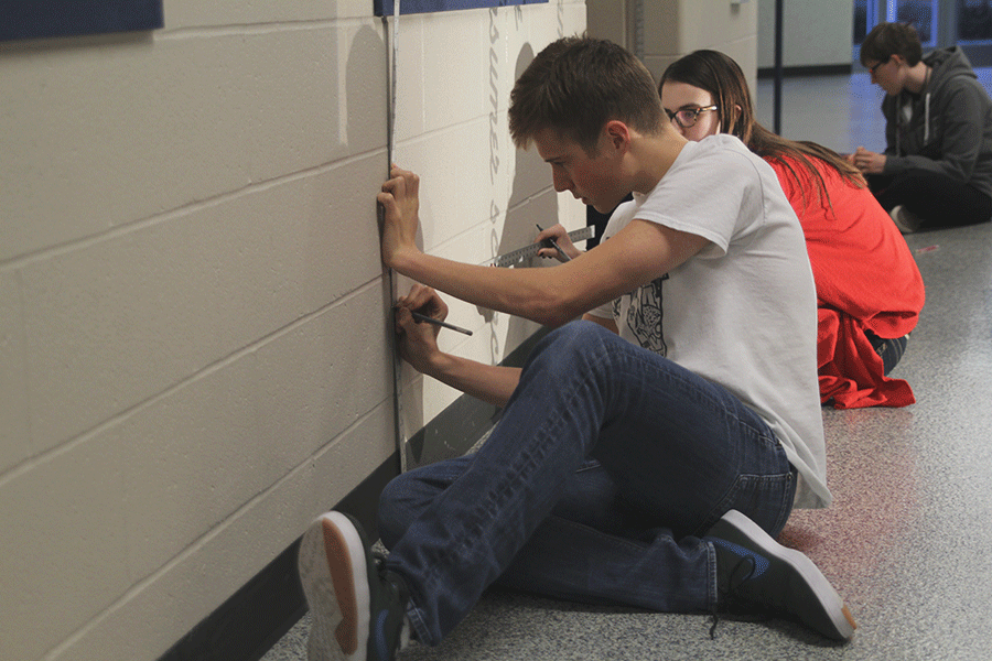 As part of an NAHS project, senior Dylan Fox begins work on a mural by tracing lines in the C-wing hallway on Thursday, Dec. 11.