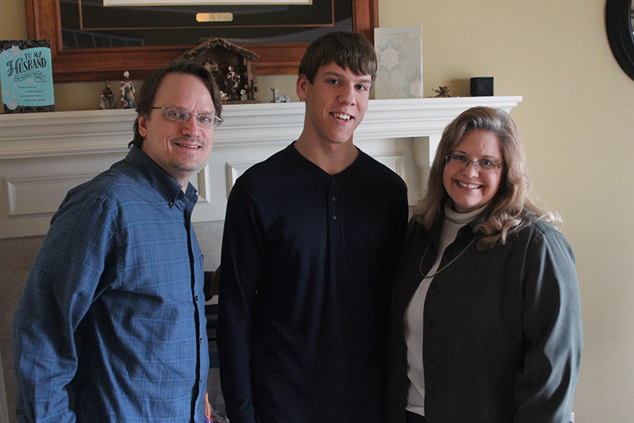 Junior Alex Martini stands with his adoptive parents, Vince and Debbie Martini in their living room on Tuesday, December 30.