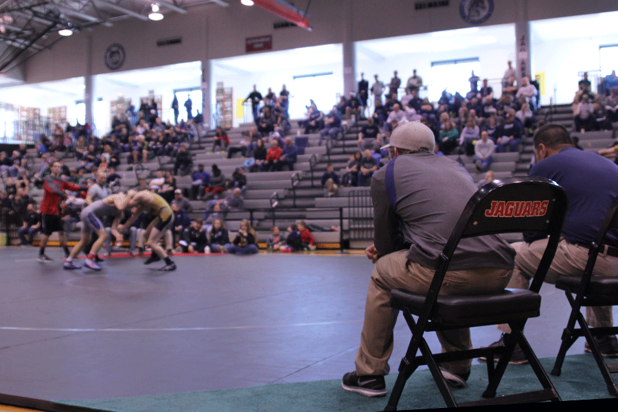 Head coach Travis Keal sits on the mat to coach his wrestlers on Saturday Feb. 21. 