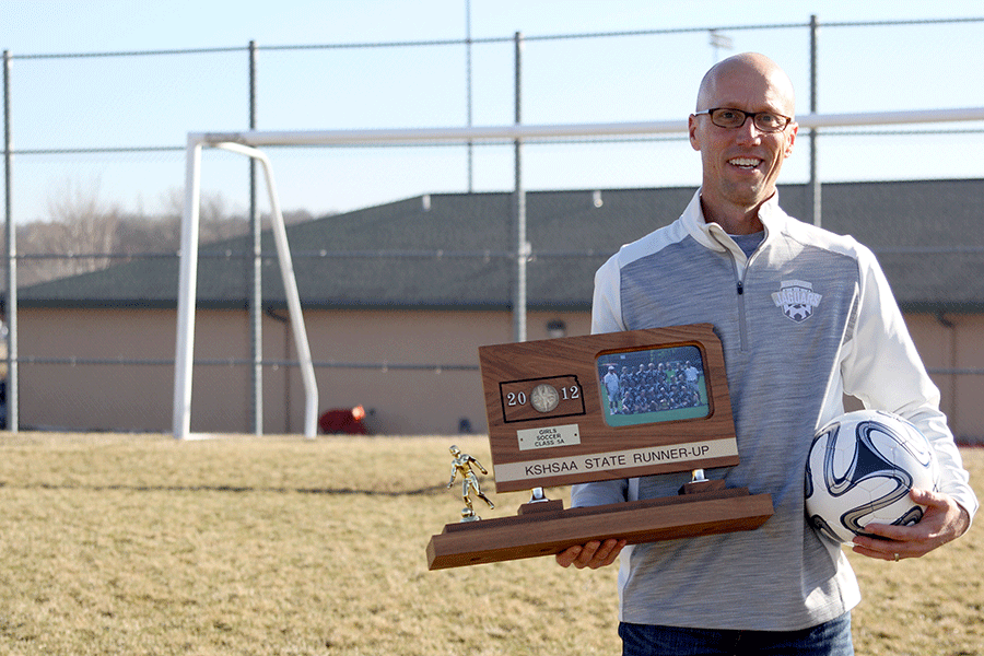 Soccer coach Arlan Vomhof holds a soccer ball and a 2012 girls soccer KSHSAA State Runner-up trophy on Friday, Feb. 6. I really like coaching girls because they are coachable, Vomhof said. I like coaching boys because of the speed of the game.