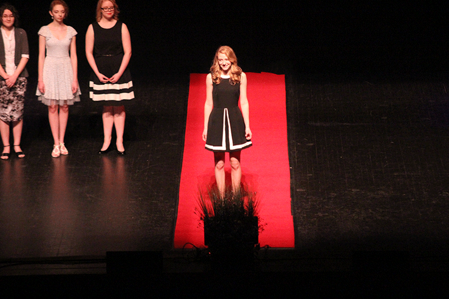 Senior Michaela Mense stands at the end of the red carpet while her vocal music audition video plays overhead.