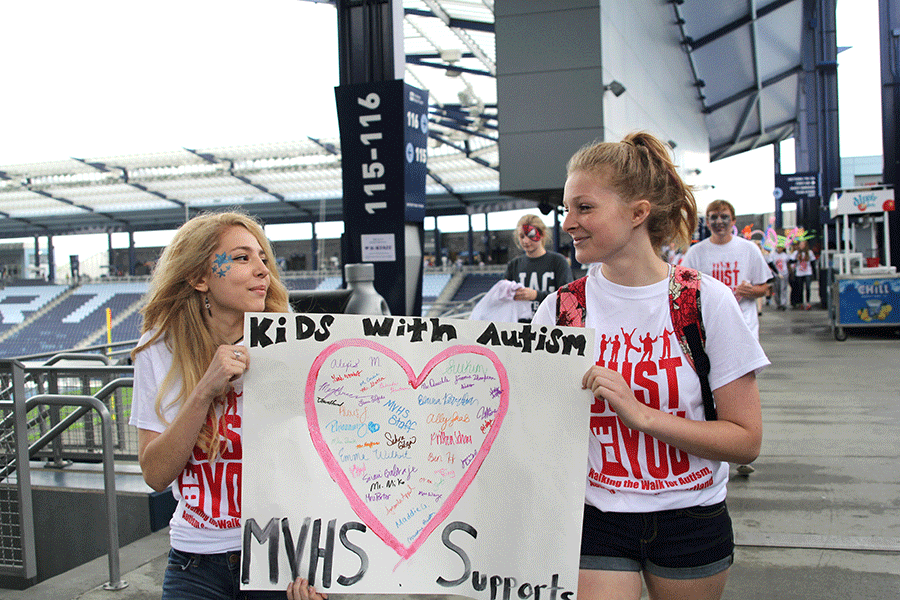 While holding a poster which is signed by students who are in MV Outreach, sophomores Emma Wilhoit and Ally Saab walk around the perimeter of the KC Sporting field. 