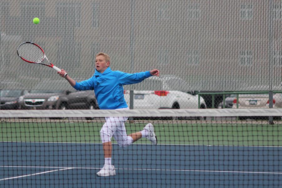Attempting to volley, freshman Dante Peterson runs to hit the ball in his singles match at a home dual against Kansas City Christian on Thursday, April 9. The boys tennis team lost the dual 2-7.