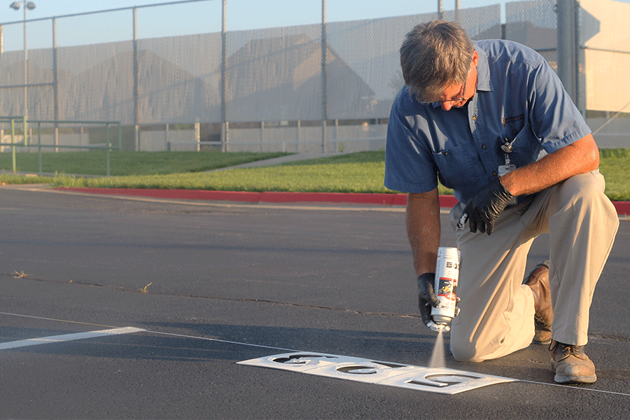 A district facilities worker spray paints numbers onto the student parking spaces for assigned parking on Thursday, July 23.