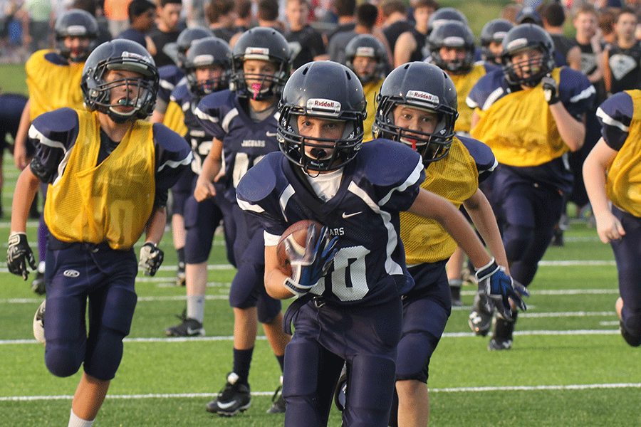 After a handoff, a Junior Football and Cheer Association football player dodges tackles for a touchdown.