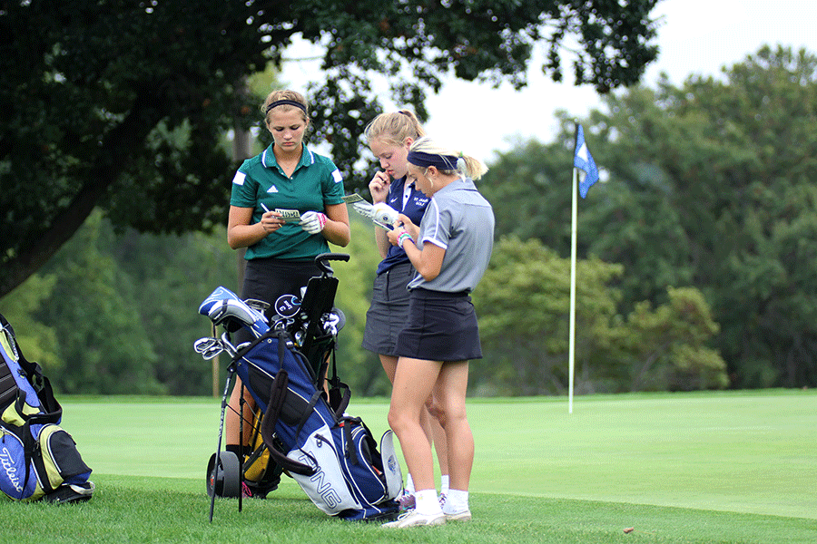 Talking with the other competitors, junior Claire Anderson counts up her strokes for the hole.
