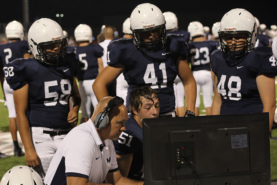 Defensive line coach Eric Thomas reviews film with some of his players on the sidelines during the football game.