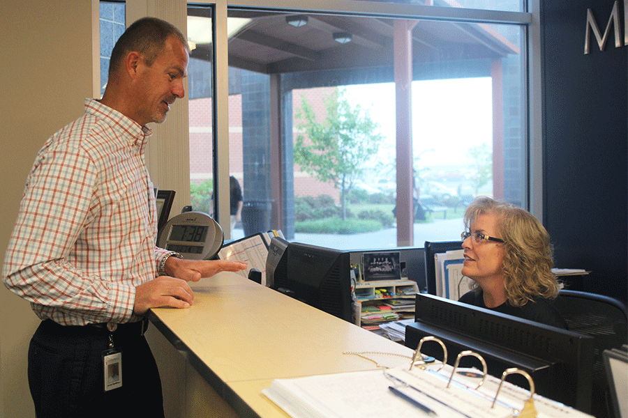 Before school starts on Tuesday, Oct. 6, athletic director Jerald VanRheen visits with secretary Lynn Bath.