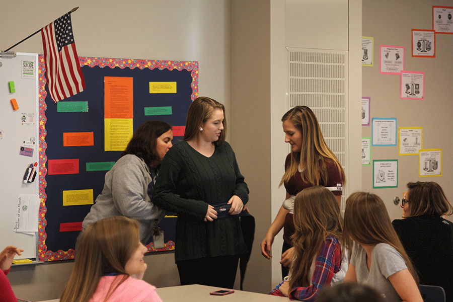 Senior Eileen Marti receives help from Family and Consumer Sciences teacher Ellee Gray while putting on an item that is supposed to remember a babys feet.