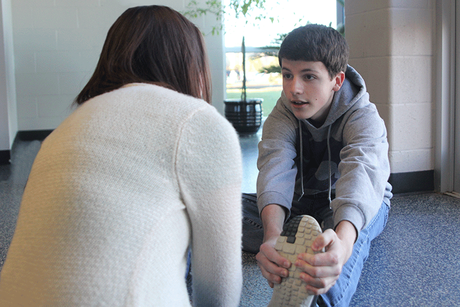 Passing time after school, sophomore Cody Robertson stretches with junior Samantha Dale as they talk about their days in the lower C hallway on Thursday, Dec. 3. Robertson, among friends, spends his time after school playing games, talking and working on homework together.