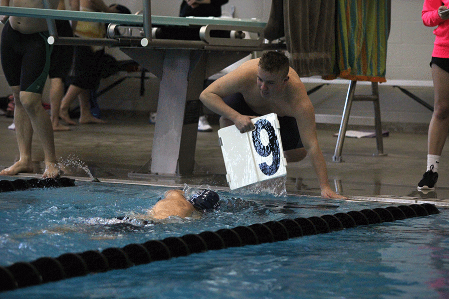 Cheering for his teammate, senior Brendan Tener pulls the lap number out of the water.