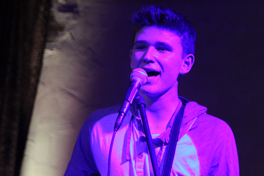 Mac Walsh sings with a purple spotlight shining on him.