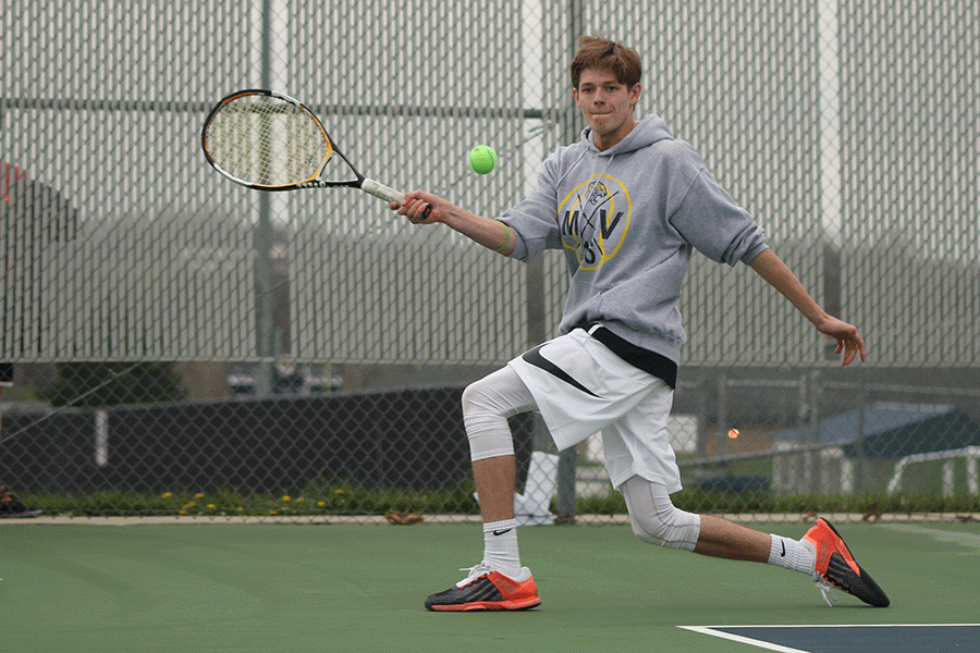 Lunging for the ball, junior Jansen McCabe follows through with a hit against his opponent from St. James.