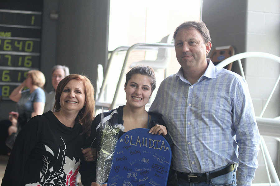 Standing with her parents, senior Claudia Meredith holds up her kick-board that was signed by the team.