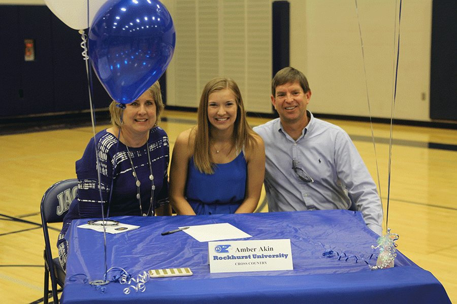 Smiling with parents, senior Amber sits down at her table decorated in Rockhurst Universitys school colors