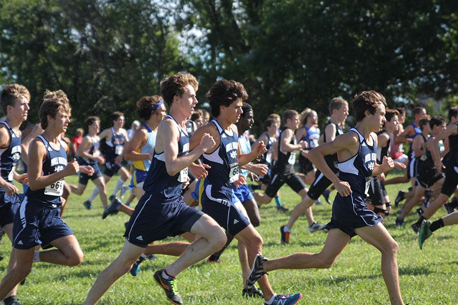 The boys varsity cross country team runs alongside each other as the race begins.