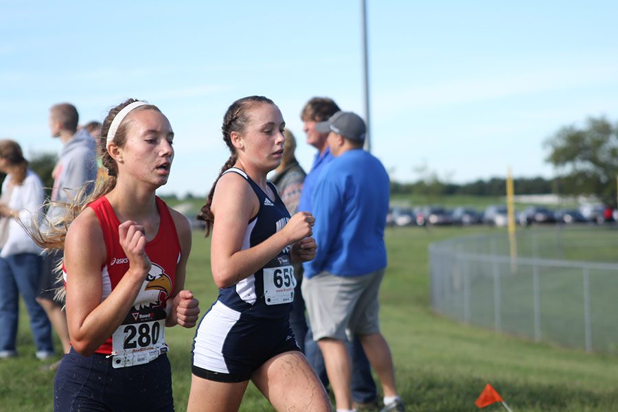 Sophomore Delaney Kemp runs side-by-side with an opponent during the 5000 meter race.