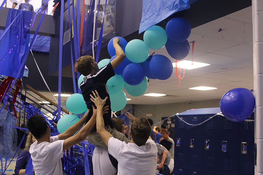 Seniors Jazz Loffredo, Tom McClain and Brady Rolig help support senior Aaron Kofoid while he decorates the ceiling.