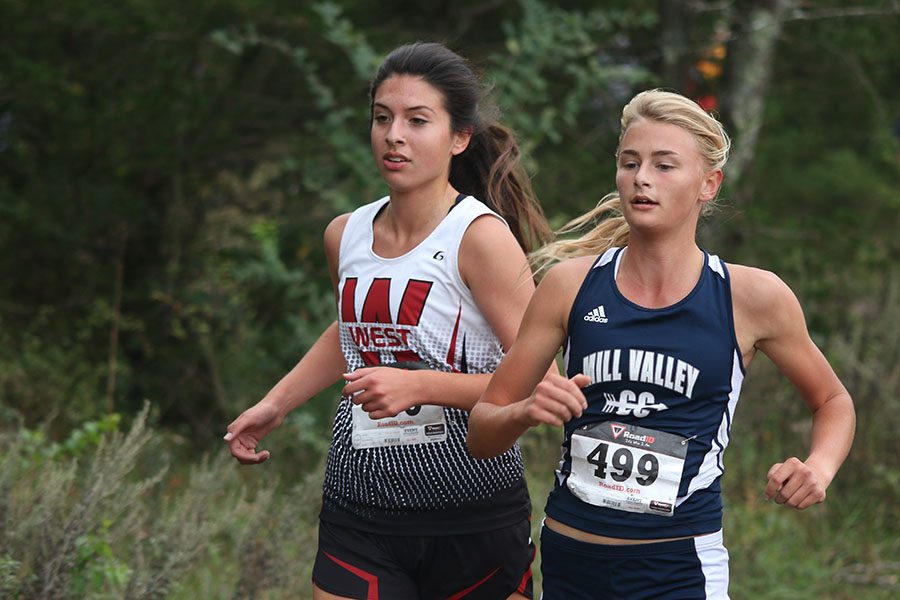 Running alongside her competitor, junior Bella Hadden races during the Eastern Kansas League meet on Thursday, Oct. 13. I feel like the team overall did well for our first year in the EKL, Hadden said. Our main goal was to beat BVSW and we edged them out by two points.