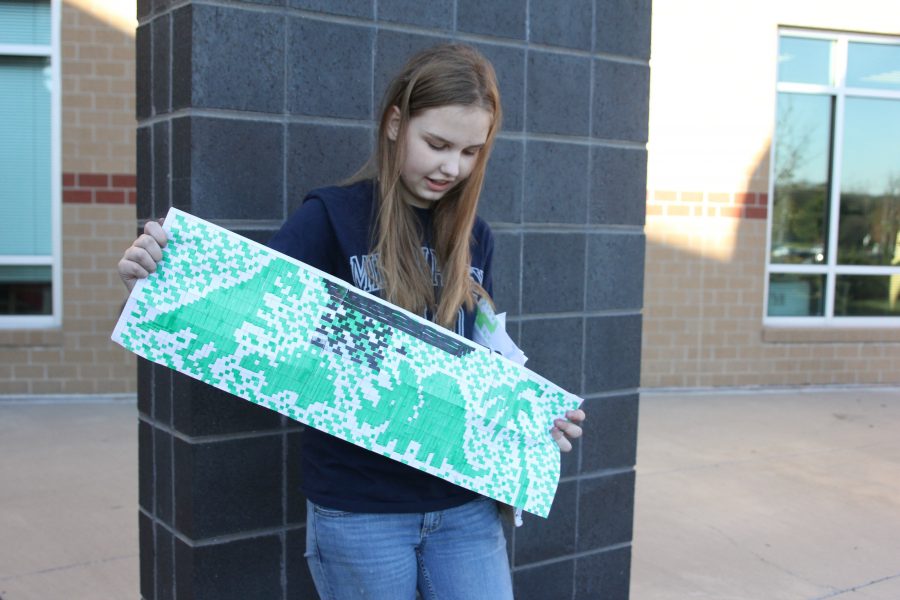 Holding her full-page graph of dinosaur designs on Wednesday, Nov. 9, junior Marissa Olin uses them as inspiration for most of the clothing and items she creates.