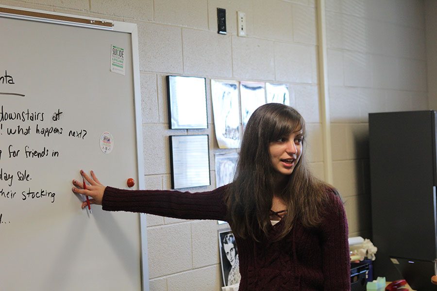 While pointing at the board during a creative writing meeting, sophomore Sarah Gawith explains the holiday writing activity.