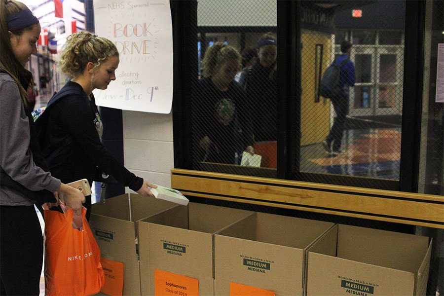 Sophomores Grace Goetsch and Sophie Friesen place their books in the box for donation. 