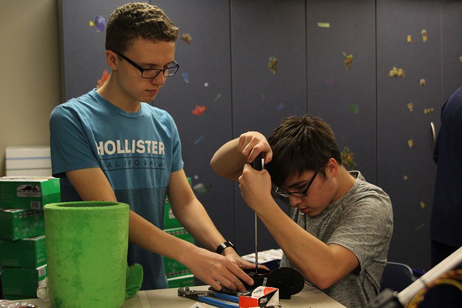 Junior Zach King holds down the base of a robot to help junior Tom Colling.