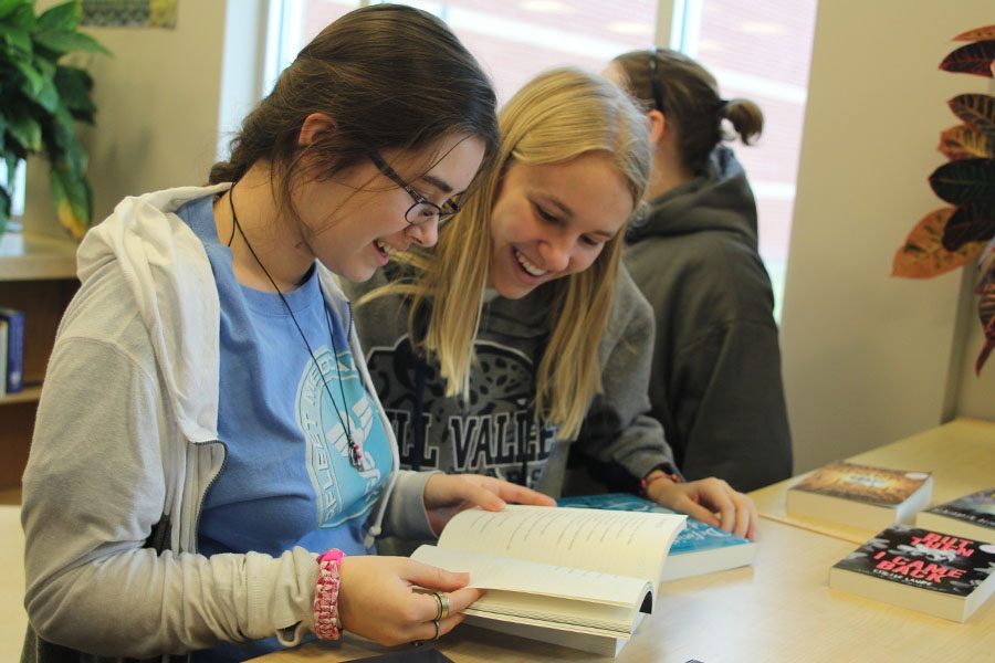 While looking at one of the books available for review, freshman Callie Roberts and freshman Joan Downey laugh in the library on Wednesday, Jan. 25.