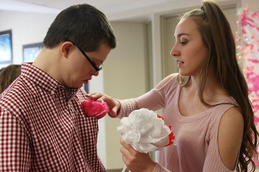 Senior Brooke Carson puts a paper flower in junior Jacob Tomandls shirt pocket.
