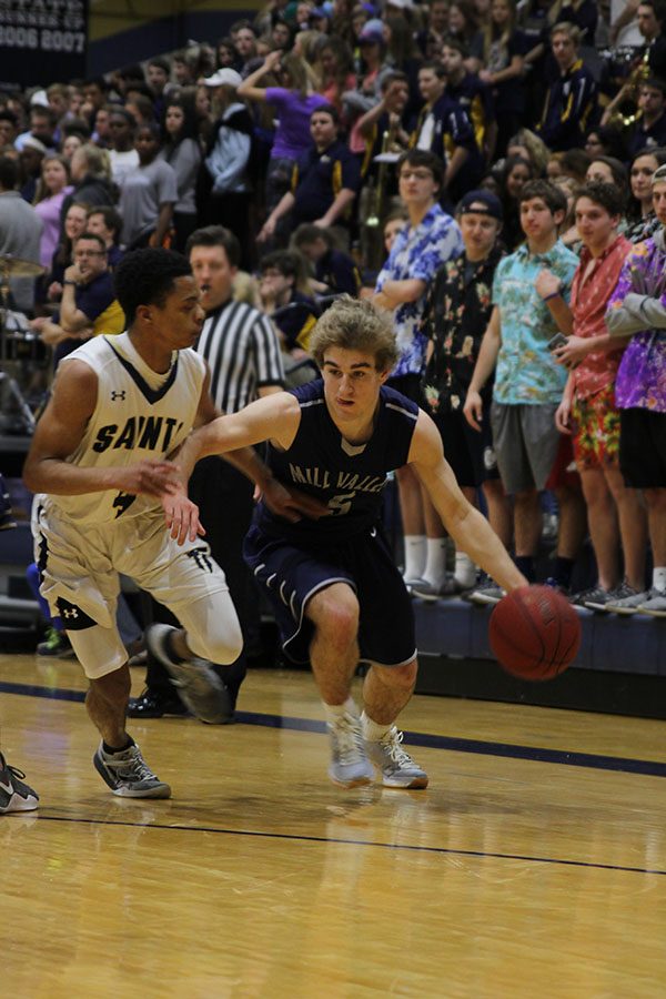 Rushing to move past a Saints defender, sophomore Logan Talley dribbles the ball.