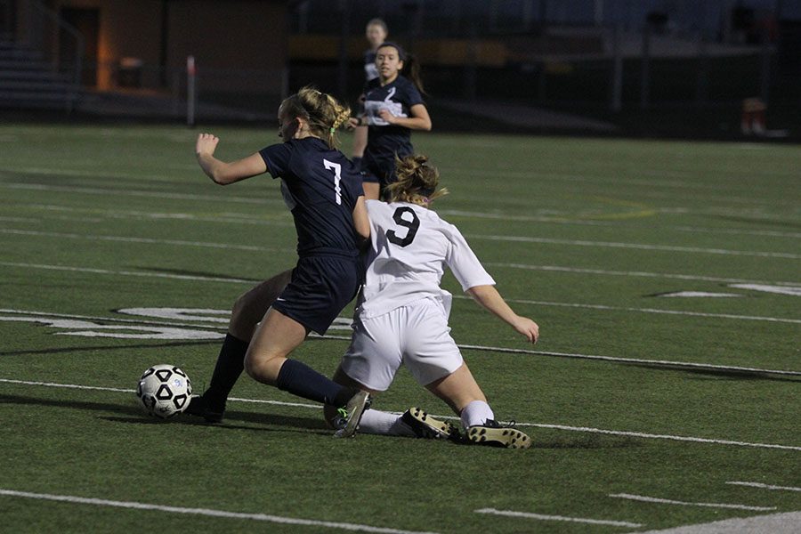 As a Blue Valley player falls to the side, junior Madison Irish holds control of the ball.
