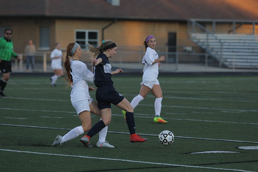 Fending off a Blue Valley player, freshman Emerson Kaiser dribbles the ball.