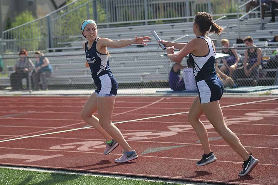 Arm outstretched, sophmore Sophia Friesen receives the relay baton from junior Brynn Rittenhouse.