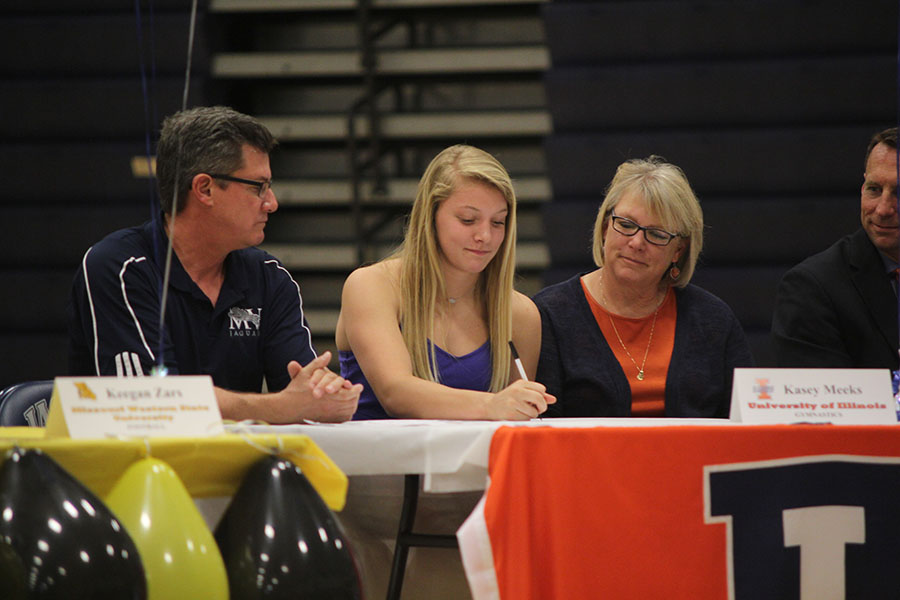 Signing her letter of intent to do gymnastics for the University of Illinois, senior Kasey Meeks smiles during the signing ceremony on May 2, 2017.