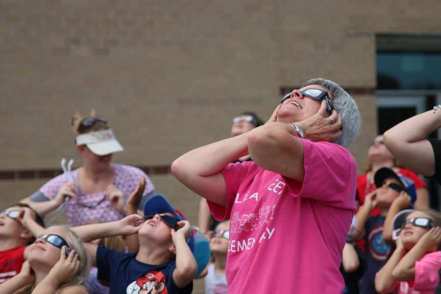 Holding onto her glasses, a second grade teacher smiles while seeing the beginning of the eclipse.