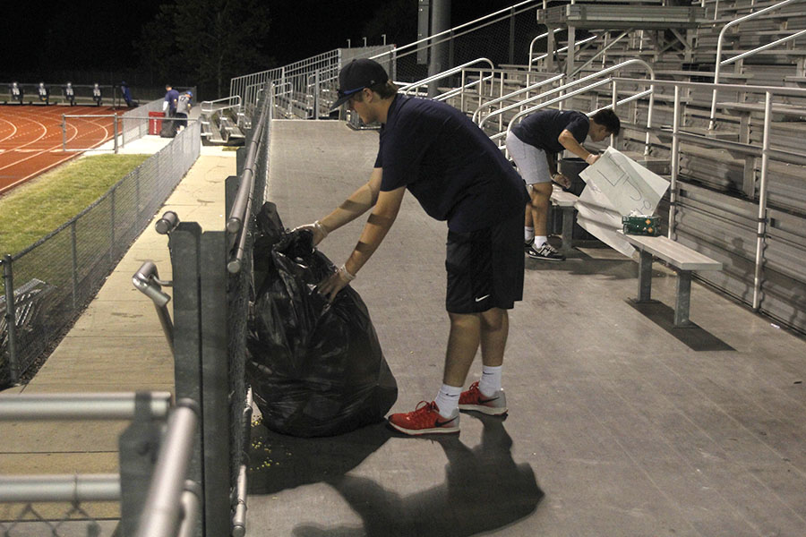 Tying up a garbage bag following the football game, junior Cole Conner cleans the bleachers on Friday, Sept. 8.