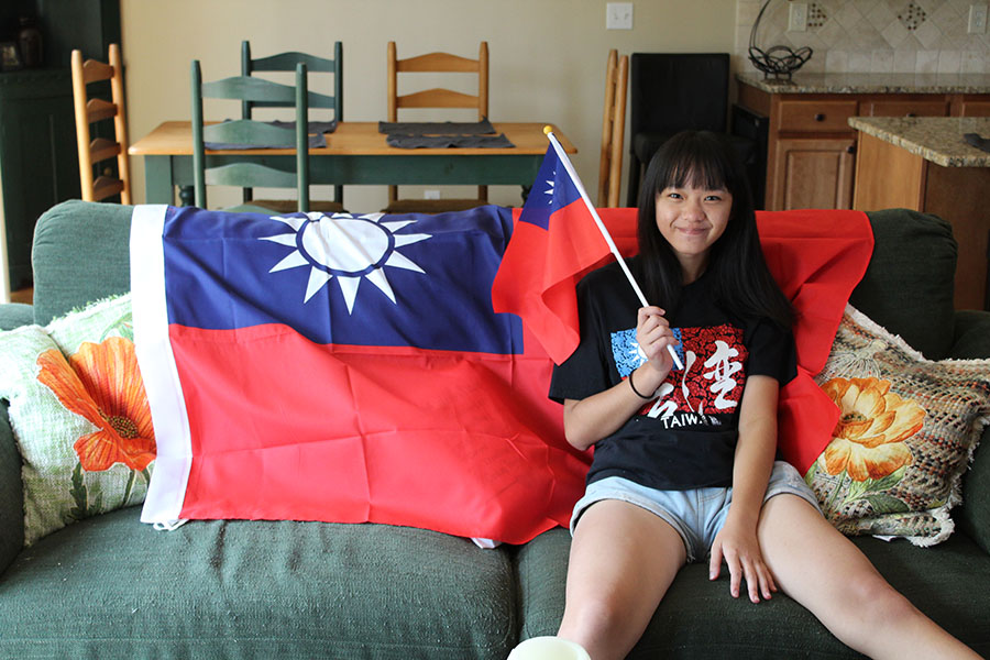 Sitting on the couch in her host family's home, foreign exchange student and senior Eunice Hsu poses in front of the Taiwanese flag while holding a flag on Monday, Sept. 4.