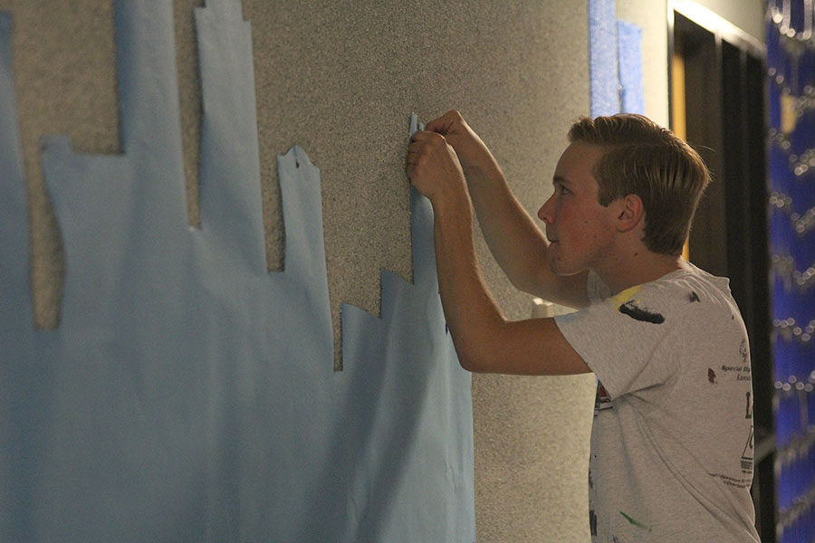 With a look of concentration on his face, senior Tyler Orbin carefully pins a cutout of the Kansas City skyline to the wall in the lower A hallway.
