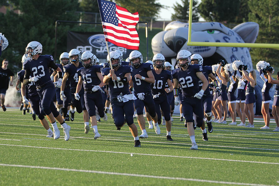 As senior Evan Rice is holding the American Flag, the football teams runs out onto the field before the homecoming game on Friday, Sept. 9.