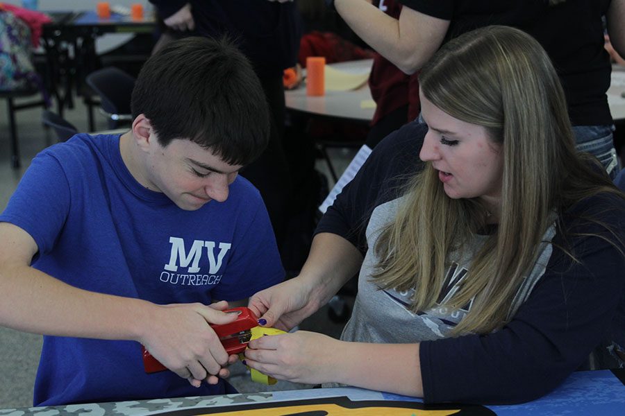 Sophomore Ashley Grega helps another student staple a stack of paper for his craft.