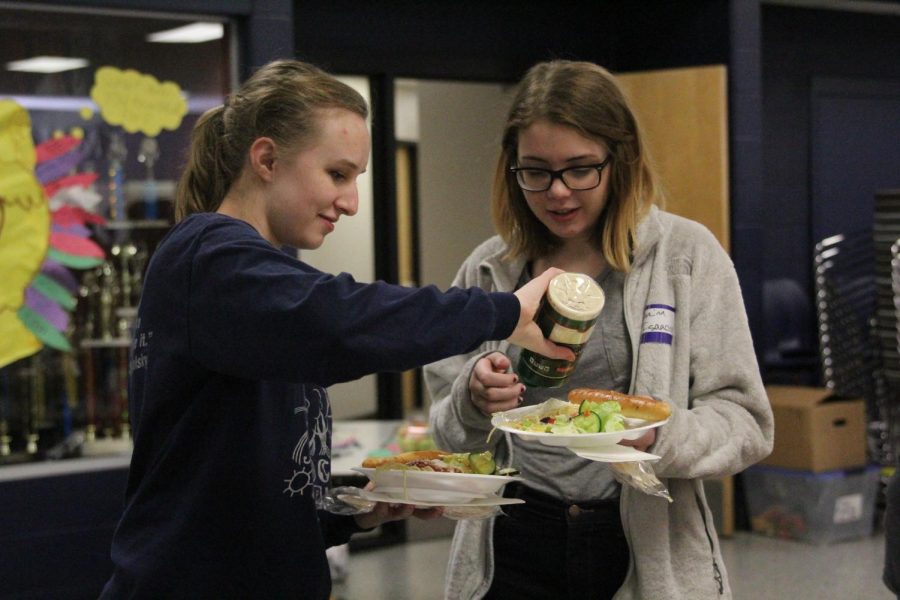 Helping a her friend sophomore Shaina Isaacsen pour cheese onto her pasta, Junior Liz Fraka joins in on the festivities durning the first ever Clubsgiving on Wednesday Nov. 15.