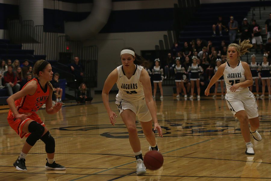 As her teammate watches her, junior Trinity Knapp dribbles towards the basket.