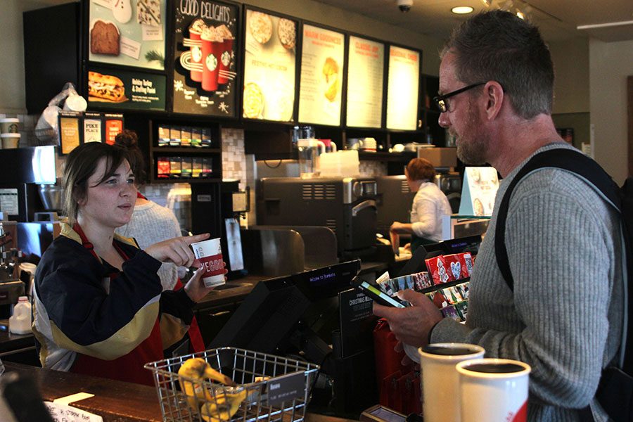After taking a customers order on Wednesday, Nov. 22, senior Kiley Beran holds out the cup to write his name on it . “I really enjoy the overall atmosphere of [Starbucks],” Beran said.  “I love the people I work with a lot.”