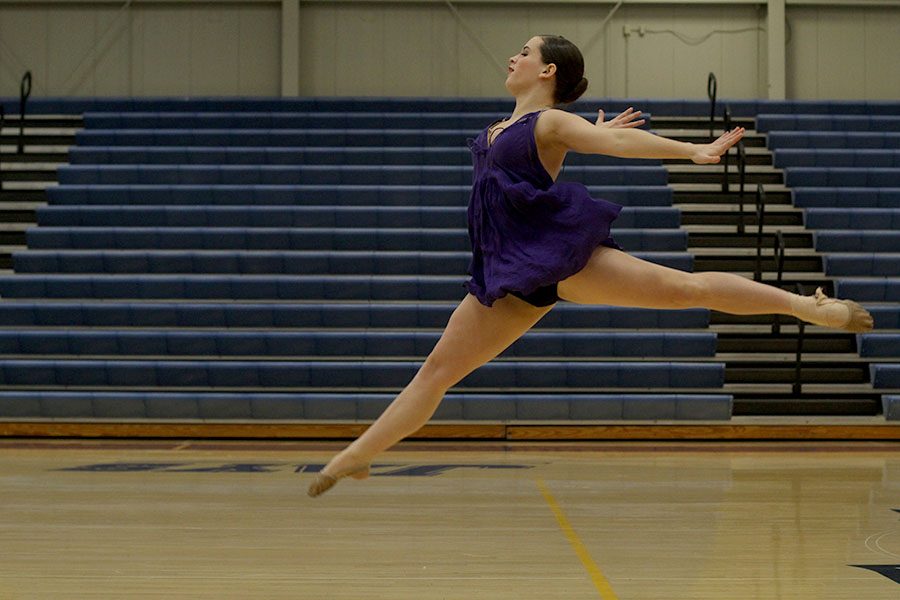 Leaping off the gym floor, junior Olivia Augustine prepares to finish her solo.