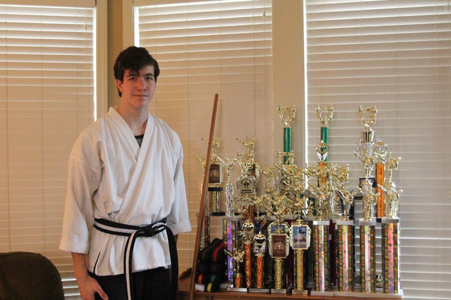 Wearing his black belt, sophomore Justin Deas stands next to trophies that he has won at numerous competitions. 