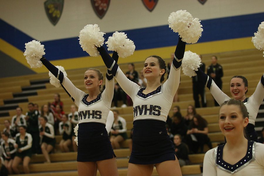 After completing the pom routine, juniors Bella Line and Olivia Augustine stand with their arms raised.