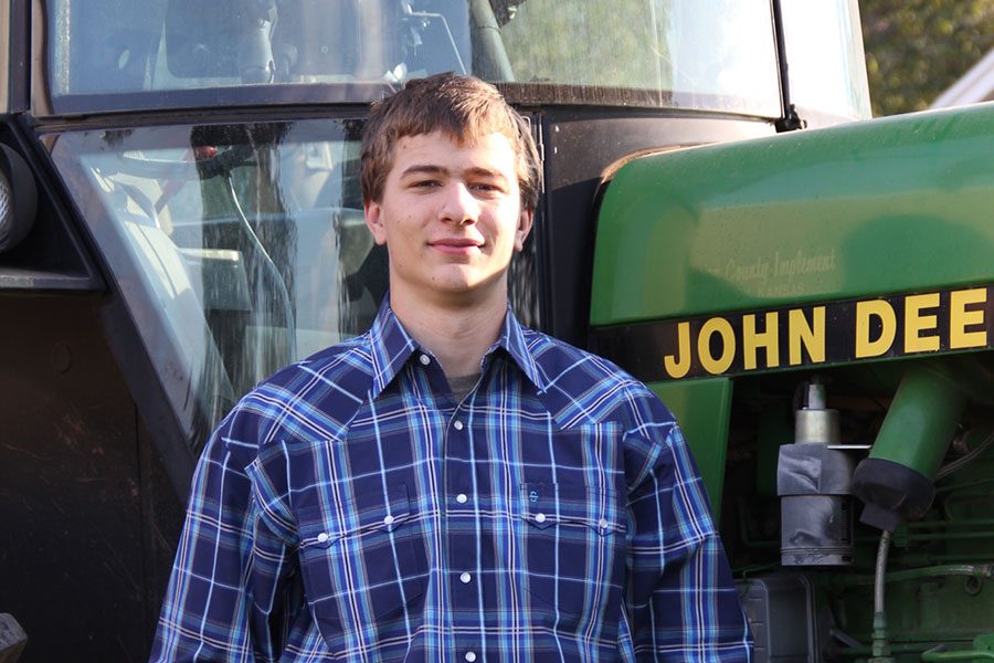 On his familys farm in Arkansas City, Kansas, senior Spencer Rahn stands in front of his tractor.